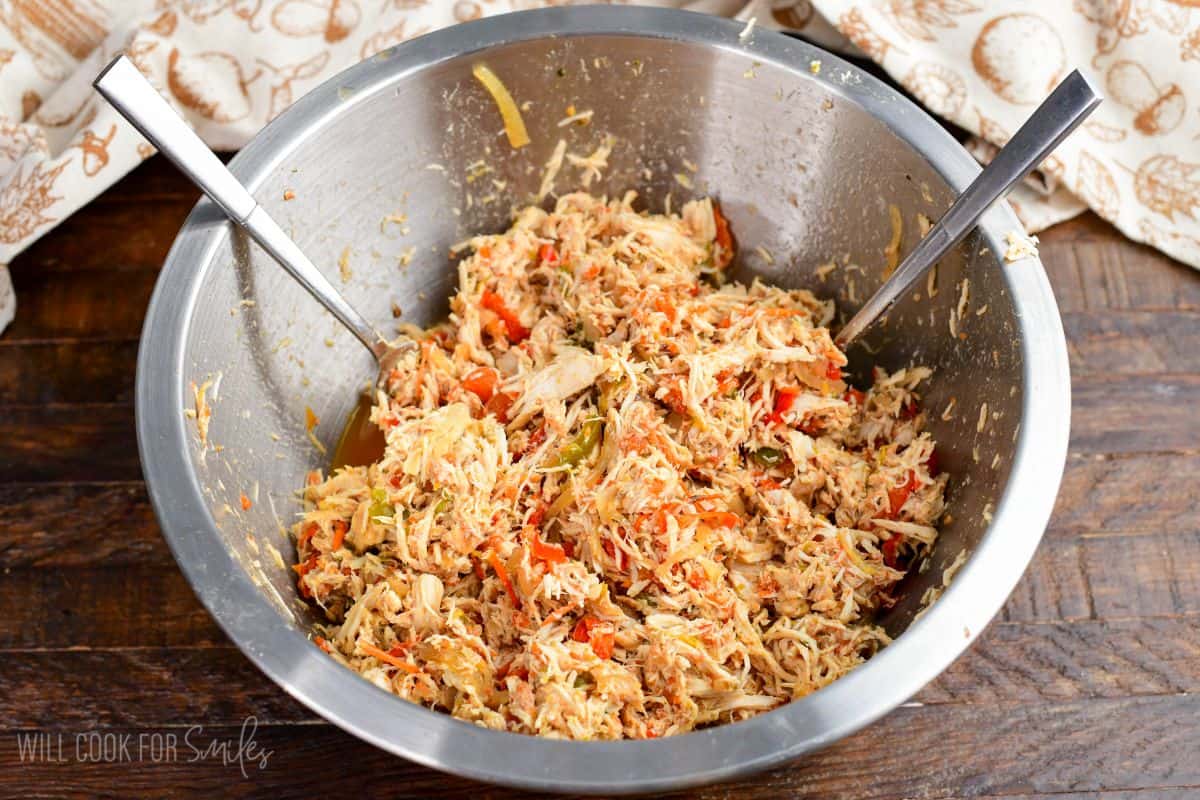Shredded crockpot salsa chicken mixed with peppers, onions, and tomatoes in a bowl with two forks.