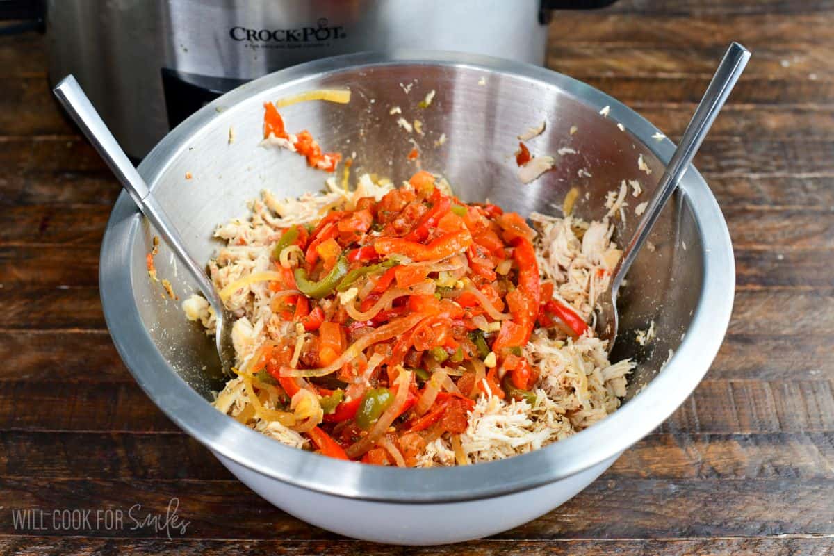 Shredded crockpot salsa chicken topped with cooked peppers, onions, and tomatoes in a bowl.