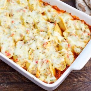 baked Italian sausage stuffed shells in the marinara sauce in a baking dish with melted cheese on top.