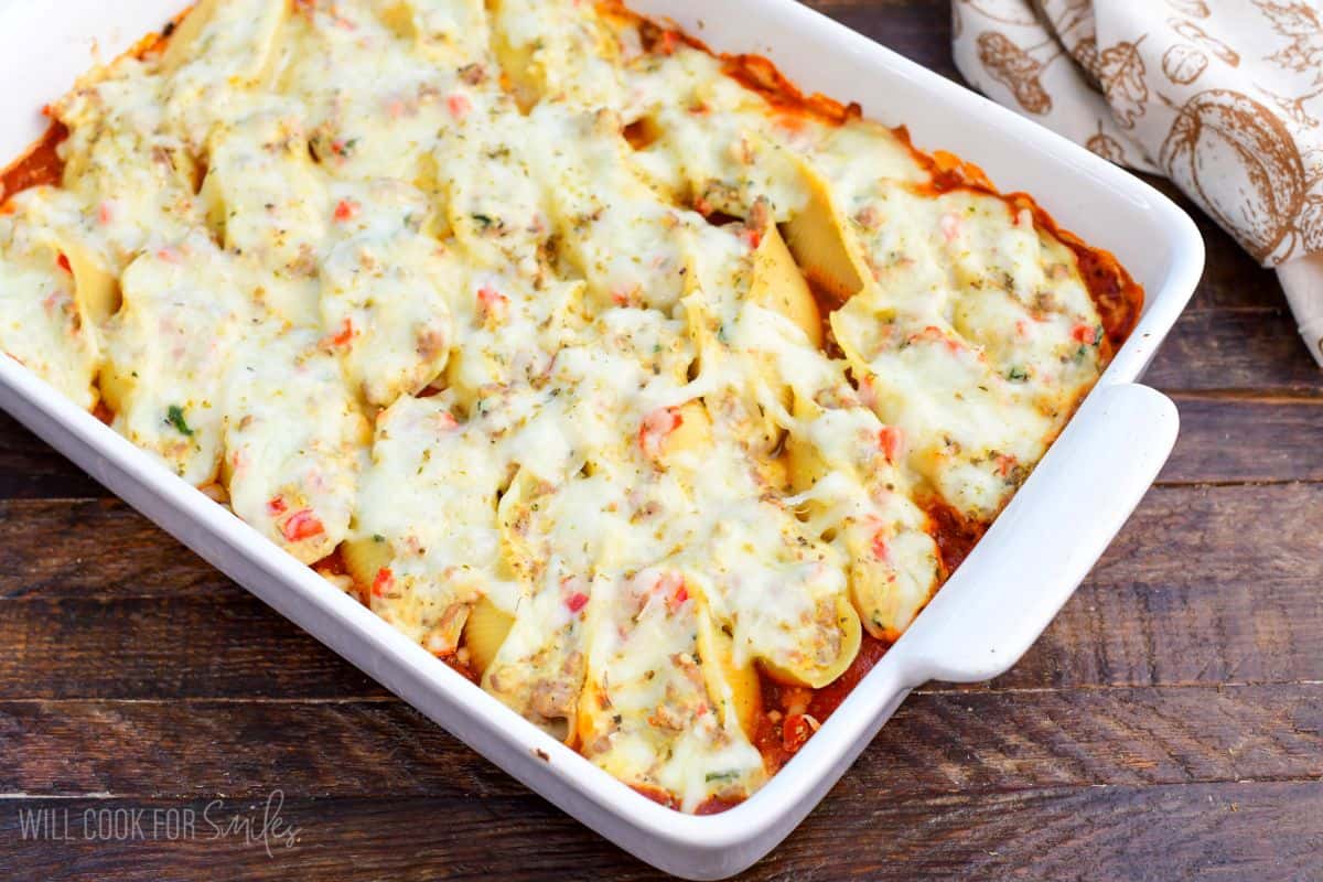 baked Italian sausage stuffed shells in the marinara sauce in a baking dish with melted cheese on top.