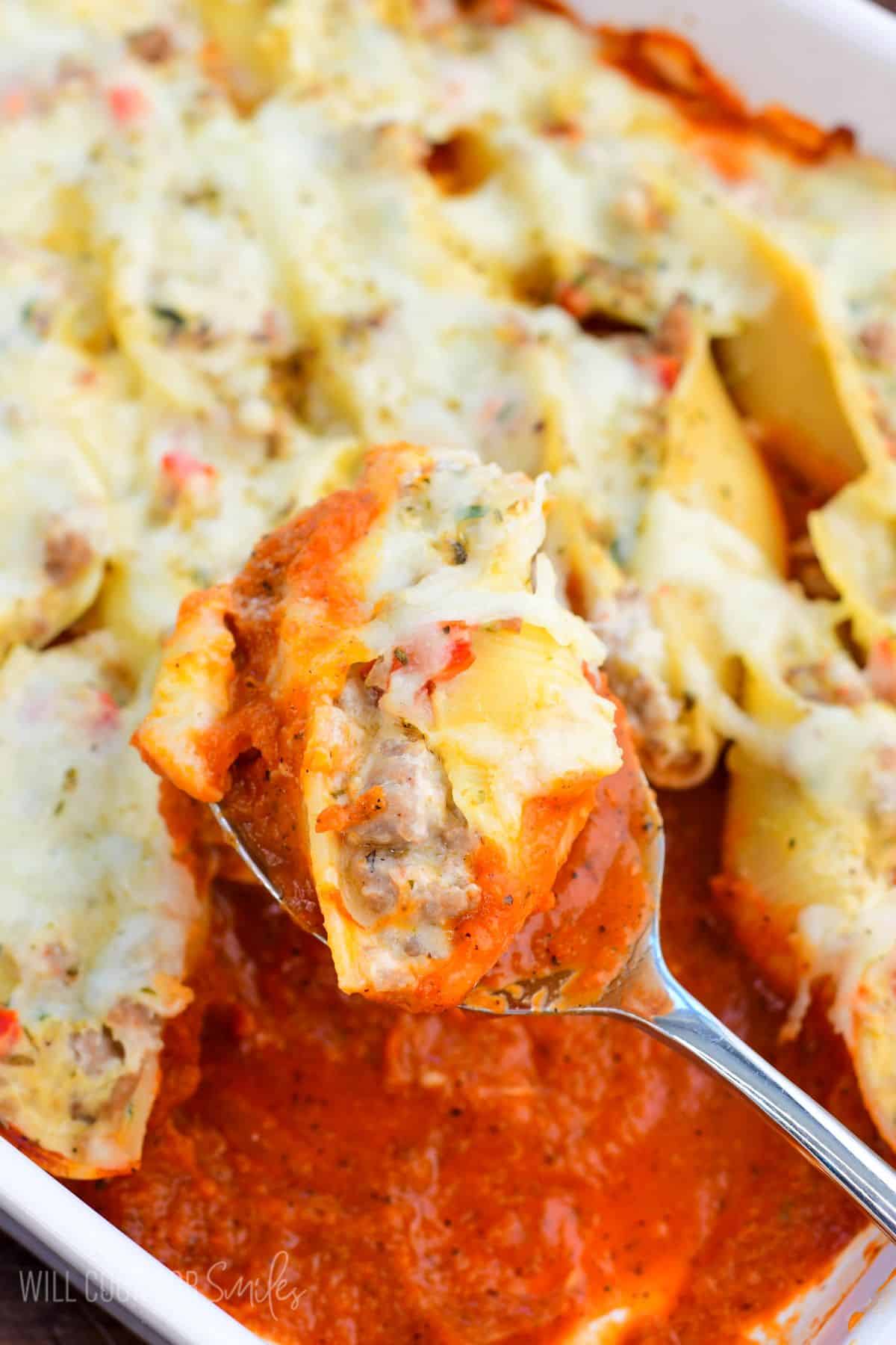 scooping out one sausage stuffed shell from the baking pan with a spoon.