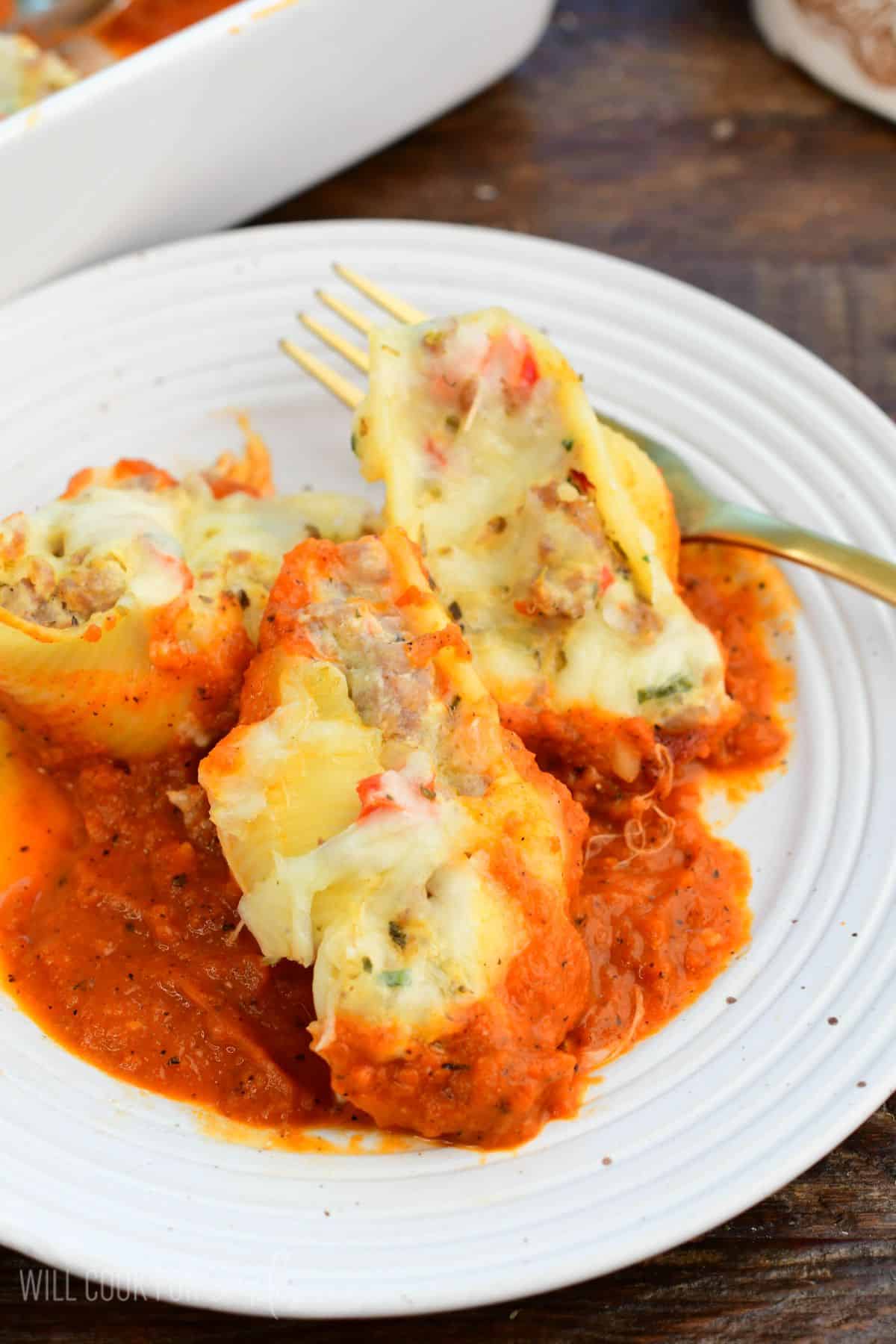 three Italian stuffed sausage shells with marinara sauce on a plate.