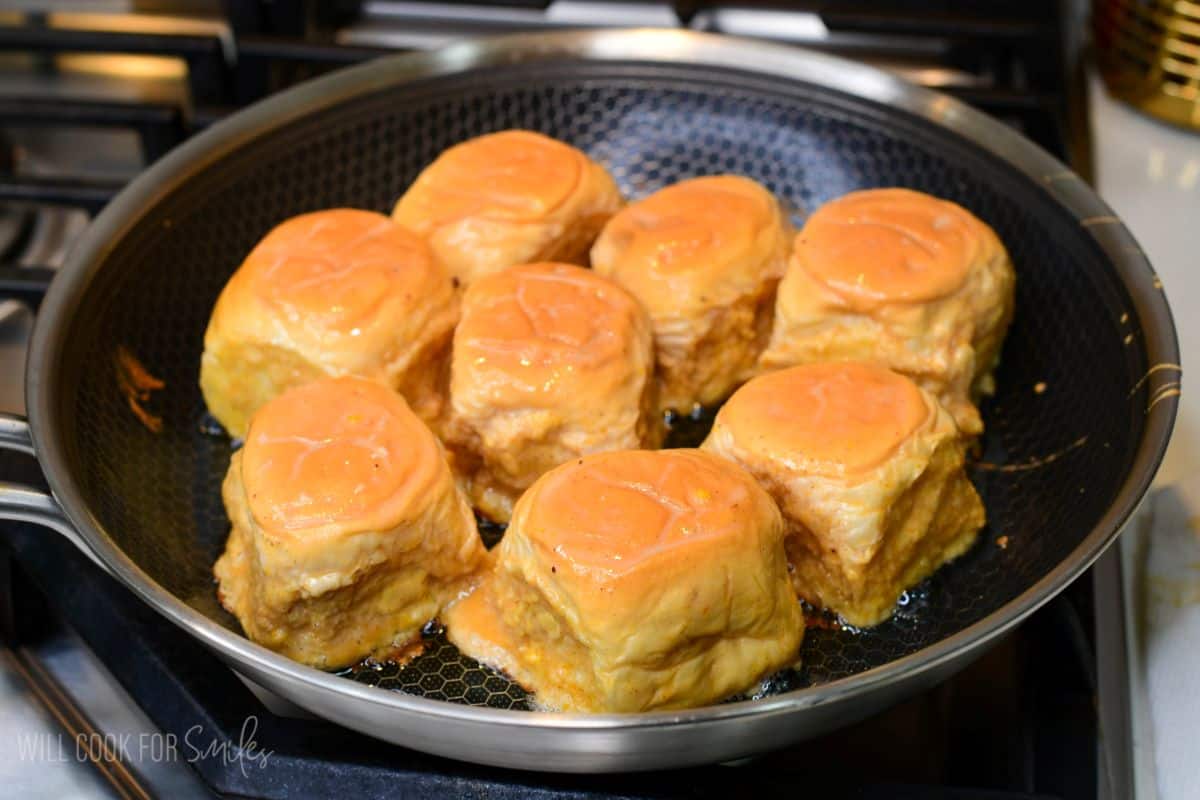 Pumpkin cheesecake stuffed Hawaiian French toast rolls cooking in a skillet until golden brown.