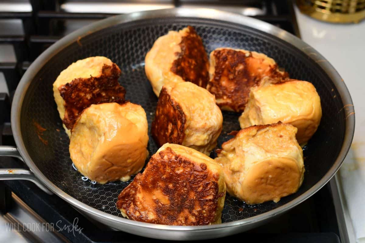 Pumpkin cheesecake stuffed Hawaiian French toast rolls cooking on all sides in a skillet until golden brown.