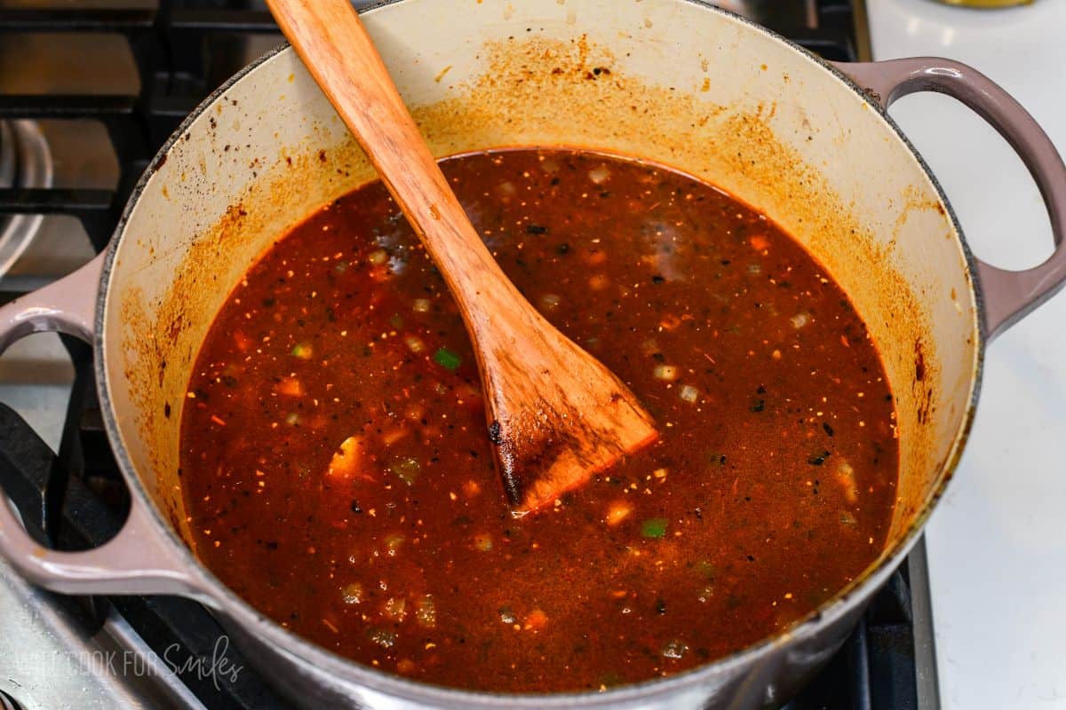 Rich, seasoned chili broth simmering with vegetables in a Dutch oven for short rib chili.