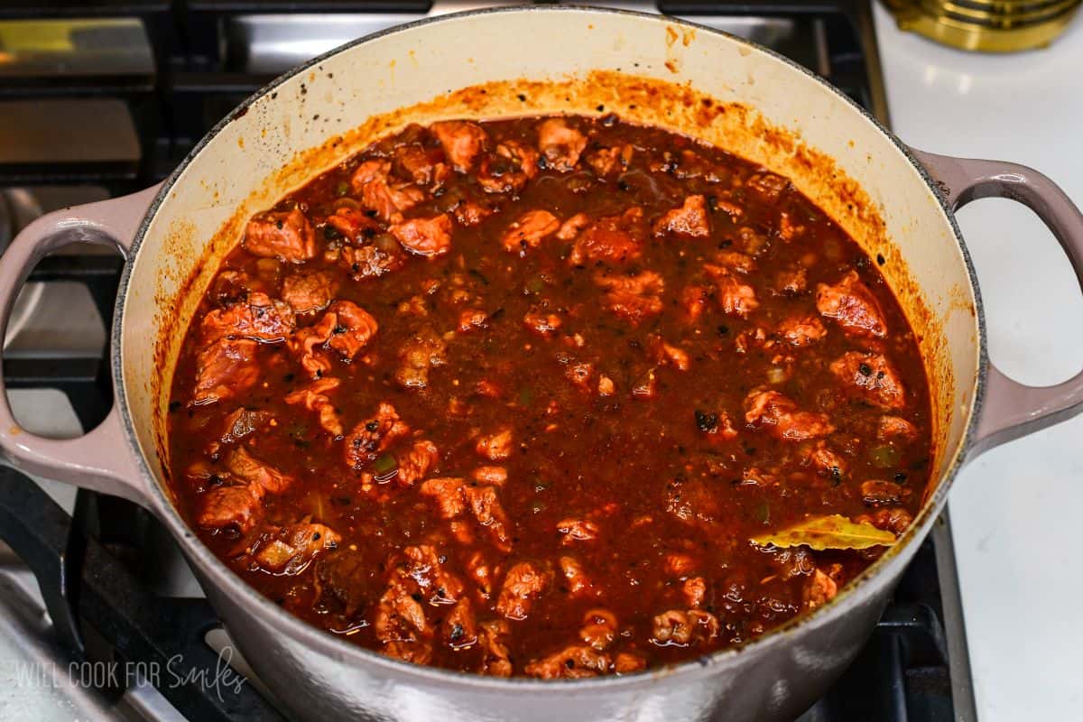 Short rib pieces simmering in a rich, seasoned chili broth in a Dutch oven.