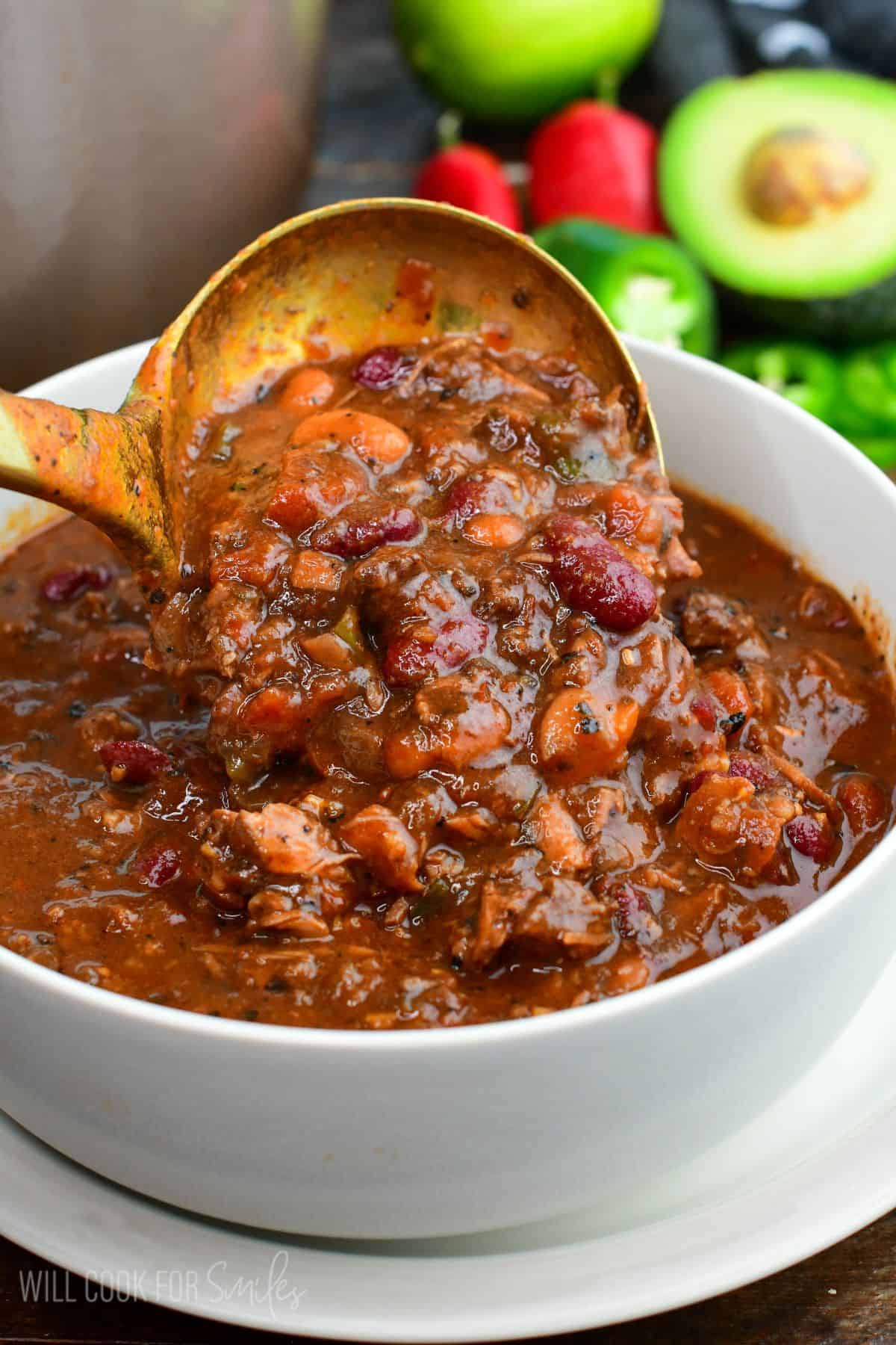 Short rib chili with tender beef and beans being ladled into a white bowl.