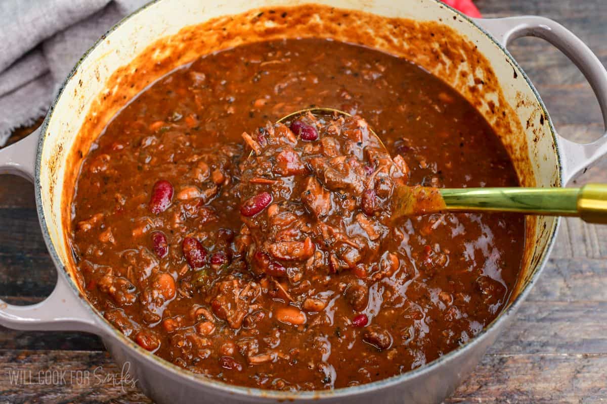 Short rib chili with tender shredded beef and beans being scooped from a Dutch oven with a ladle.