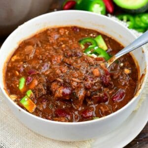 Short rib chili with tender beef and beans being scooped from a bowl topped with avocado and jalapeños.